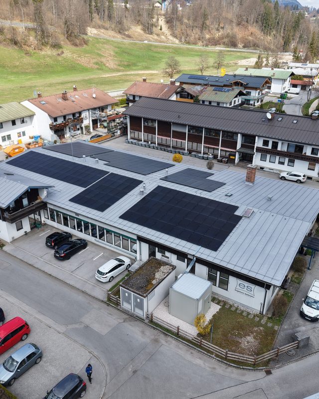 Luftaufnahme eines Firmengebäudes mit Photovoltaikanlage auf dem Dach und parkenden Autos im Außenbereich.