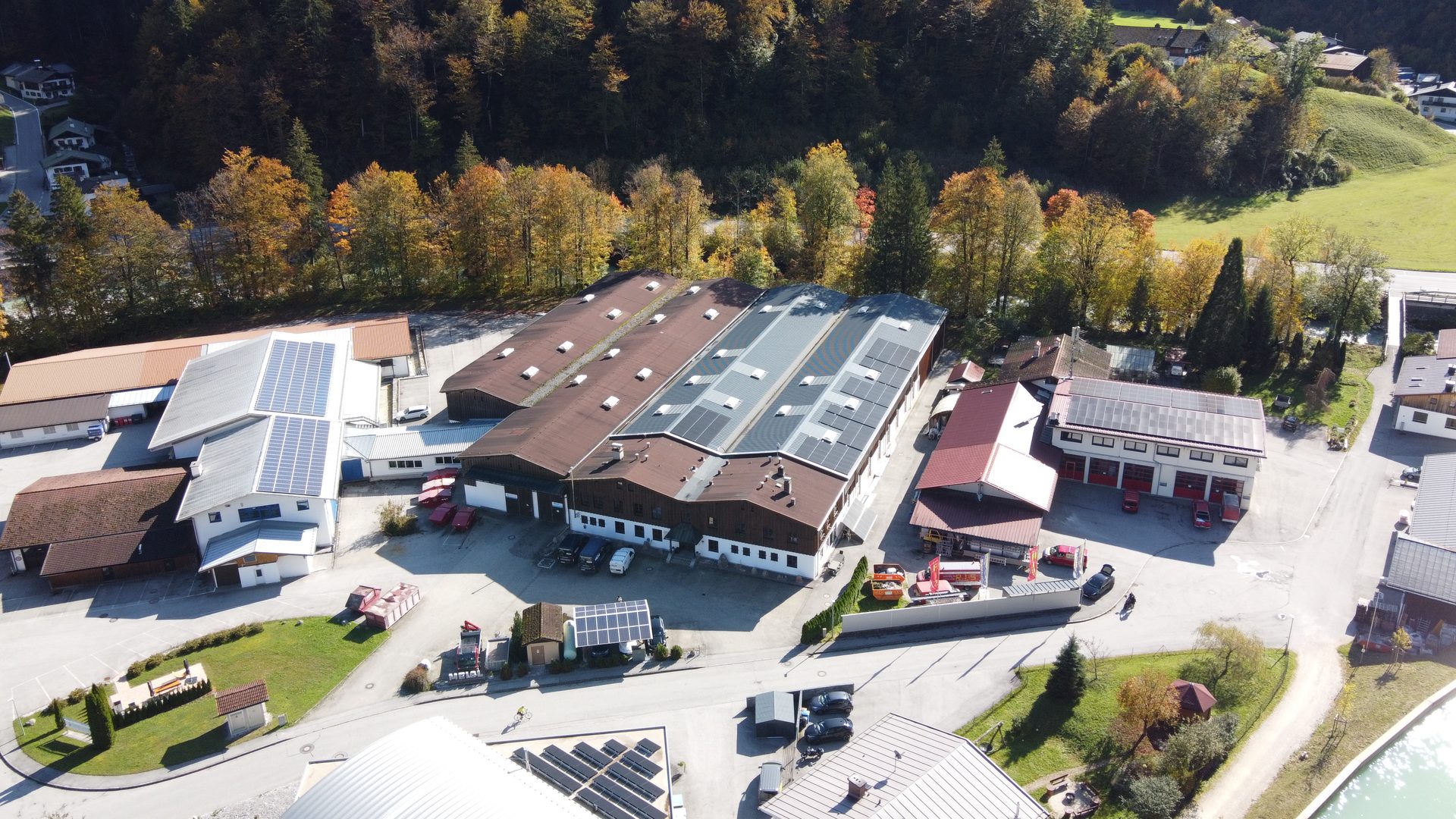 Luftaufnahme eines Betriebsgeländes mit Hallen, Dach-Solaranlagen und umgebendem Wald.