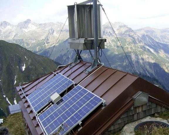 Solarmodule auf dem Dach einer Berghütte vor einer alpinen Berglandschaft.