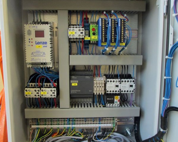 Geöffneter Schaltschrank mit Steuerungskomponenten, Kabeln, Klemmen und elektrischen Modulen.