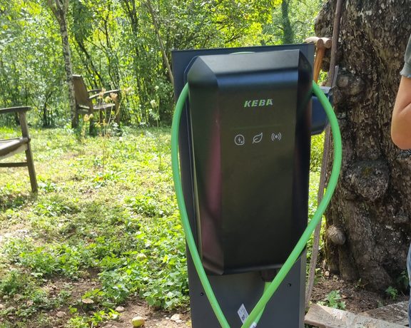 KEBA-Ladestation mit grünem Ladekabel auf einem Betonfundament im Außenbereich.