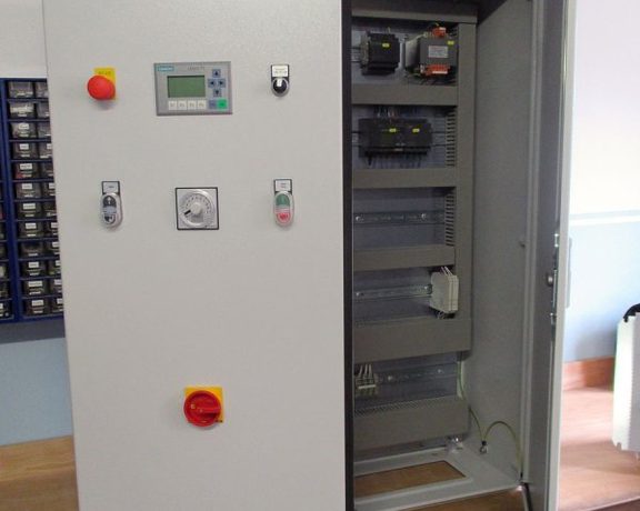 Geöffneter Schaltschrank mit Bedienpanel, Schaltern und elektrischen Komponenten auf einer Werkbank.