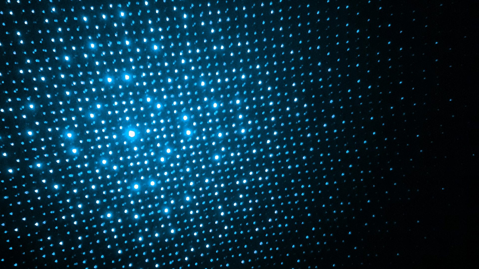 Blaues Lichtmuster aus vielen kleinen leuchtenden Punkten auf dunklem Hintergrund.